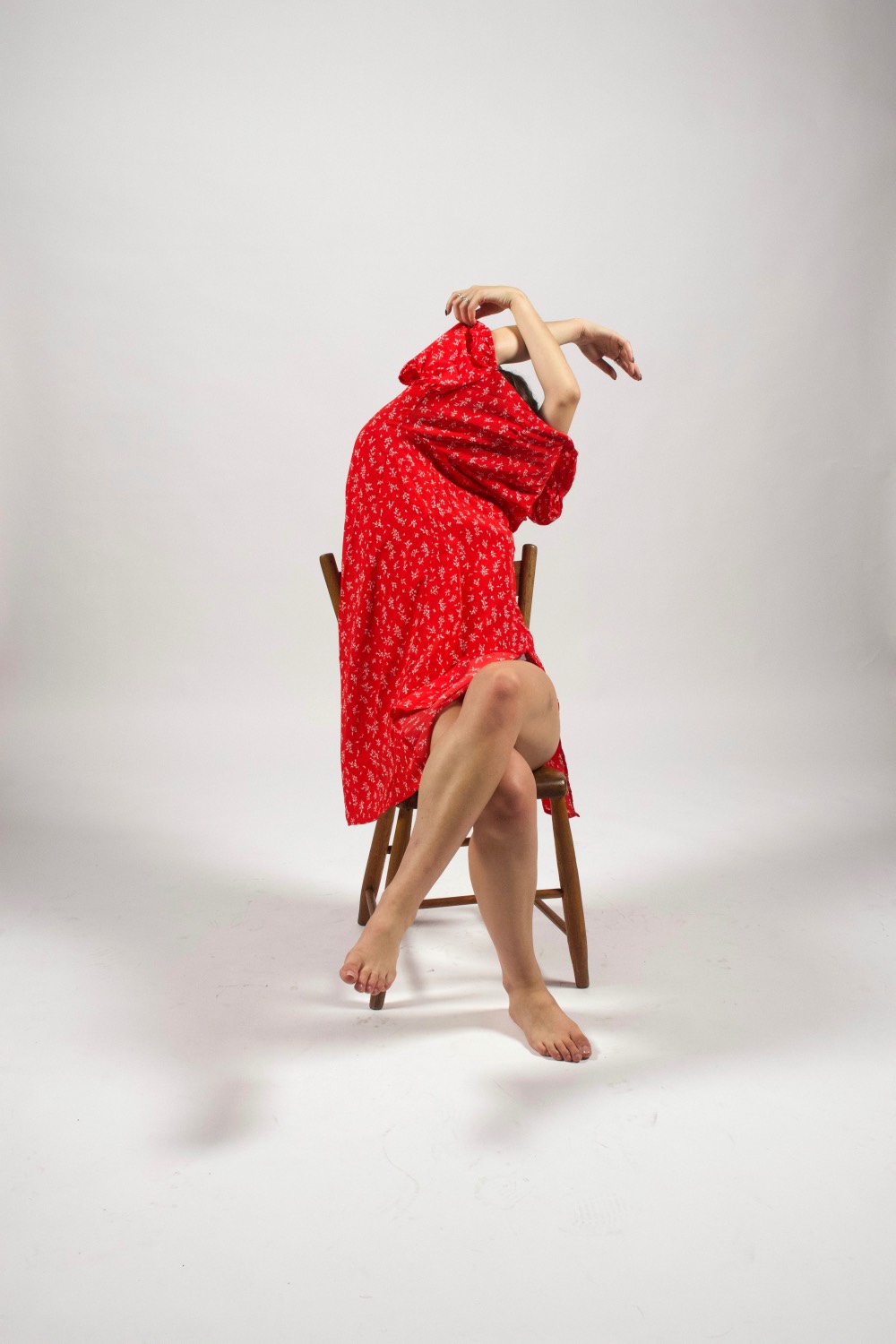 A sitting woman removing a red dress over her head.